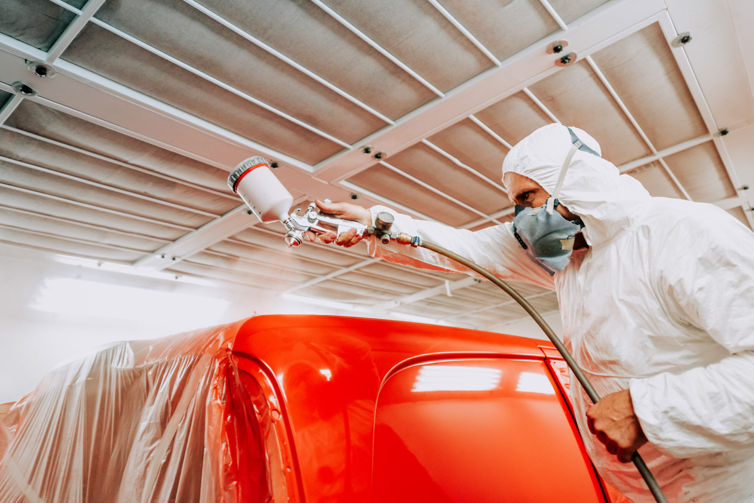 Automotive mechanical engineer painting the body of a red car with special suit at Paint and Body Shops.