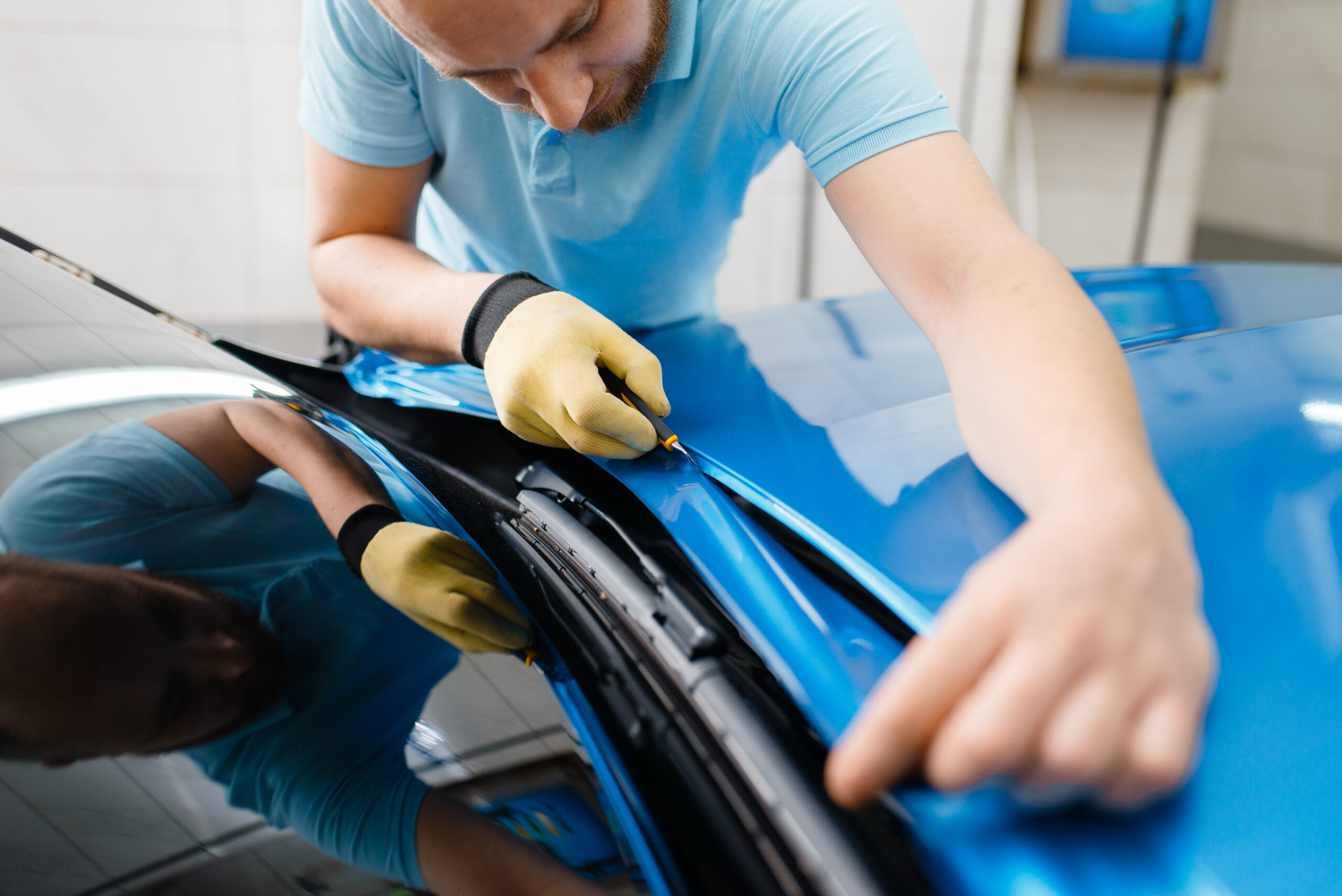 Car wrapping, man cuts protective foil or film vehicle wrapping.