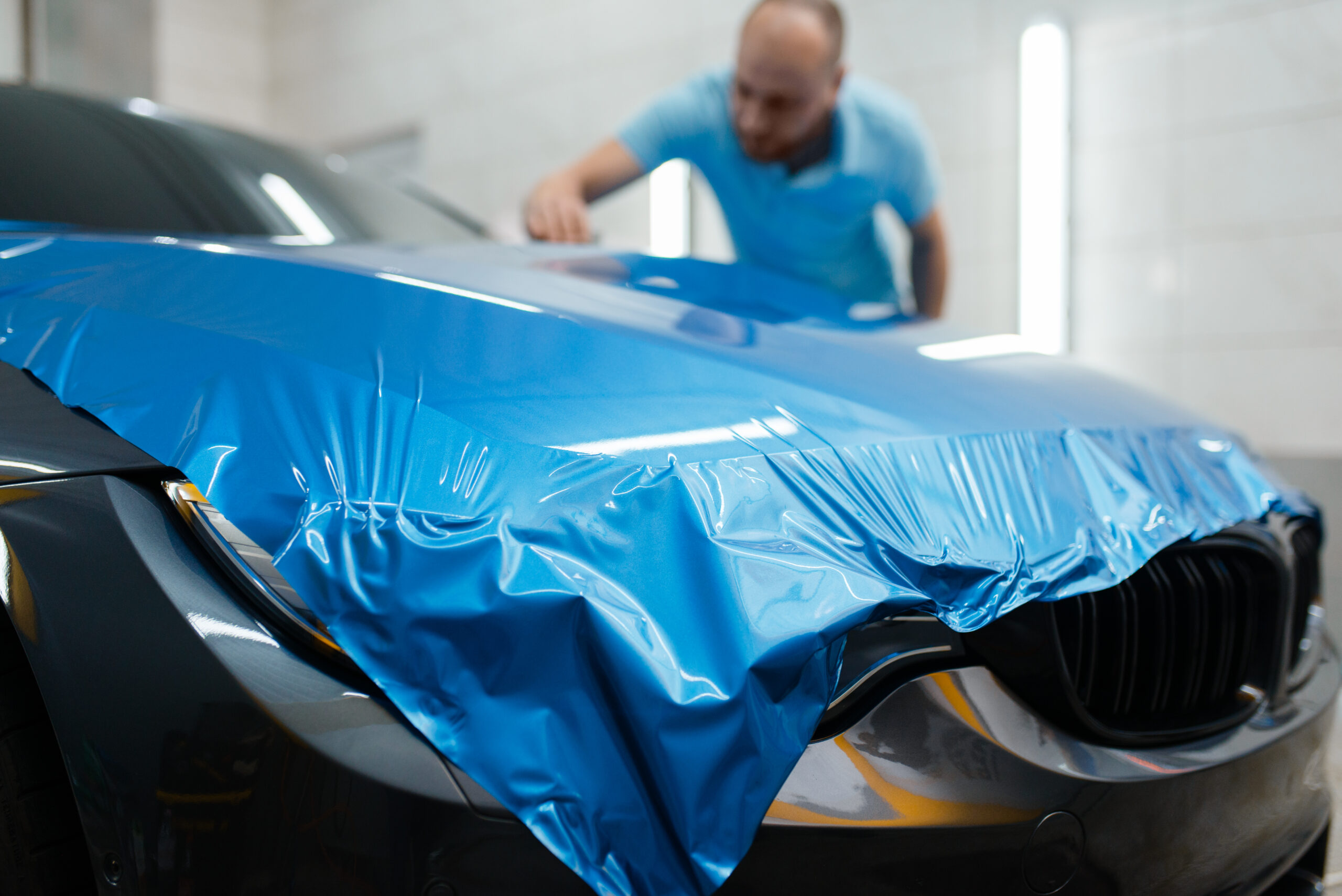 Car wrapping, man installs protective vinyl foil vehicle wrapping.