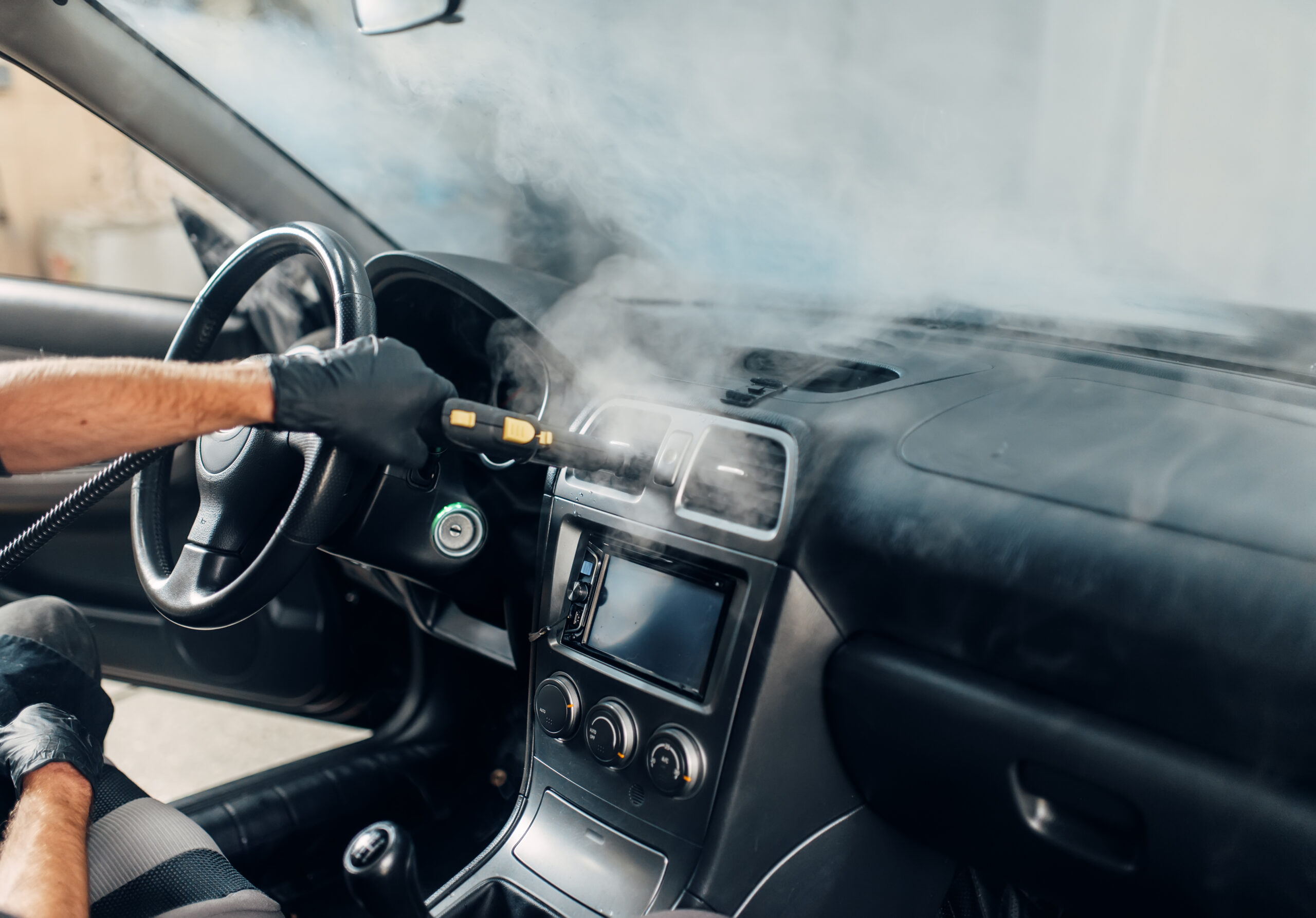 Mobile car wash, worker cleans salon with steam cleaner