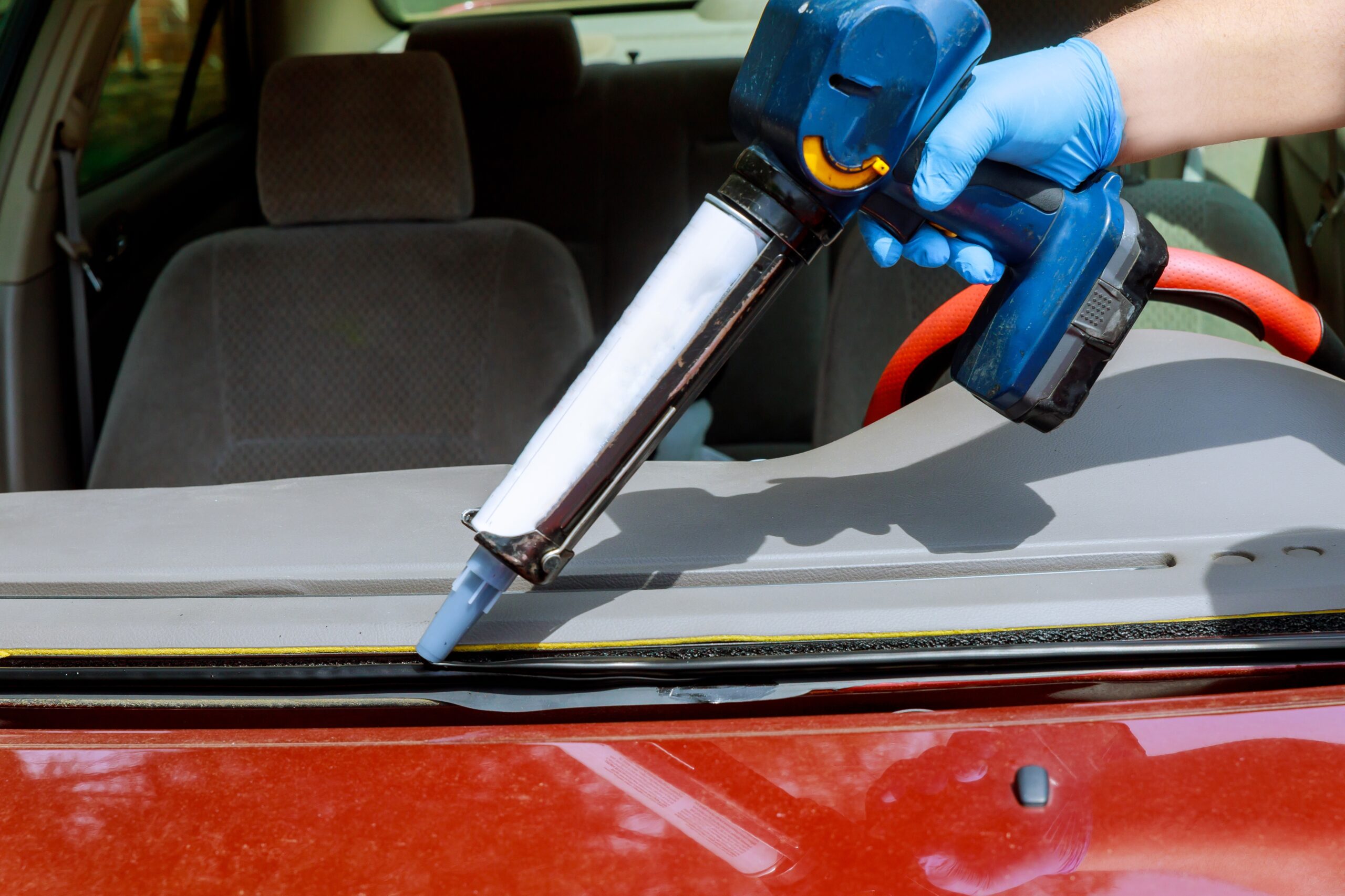 Close up car glaze worker silicone glue a windshield replacement of a car at a service station.