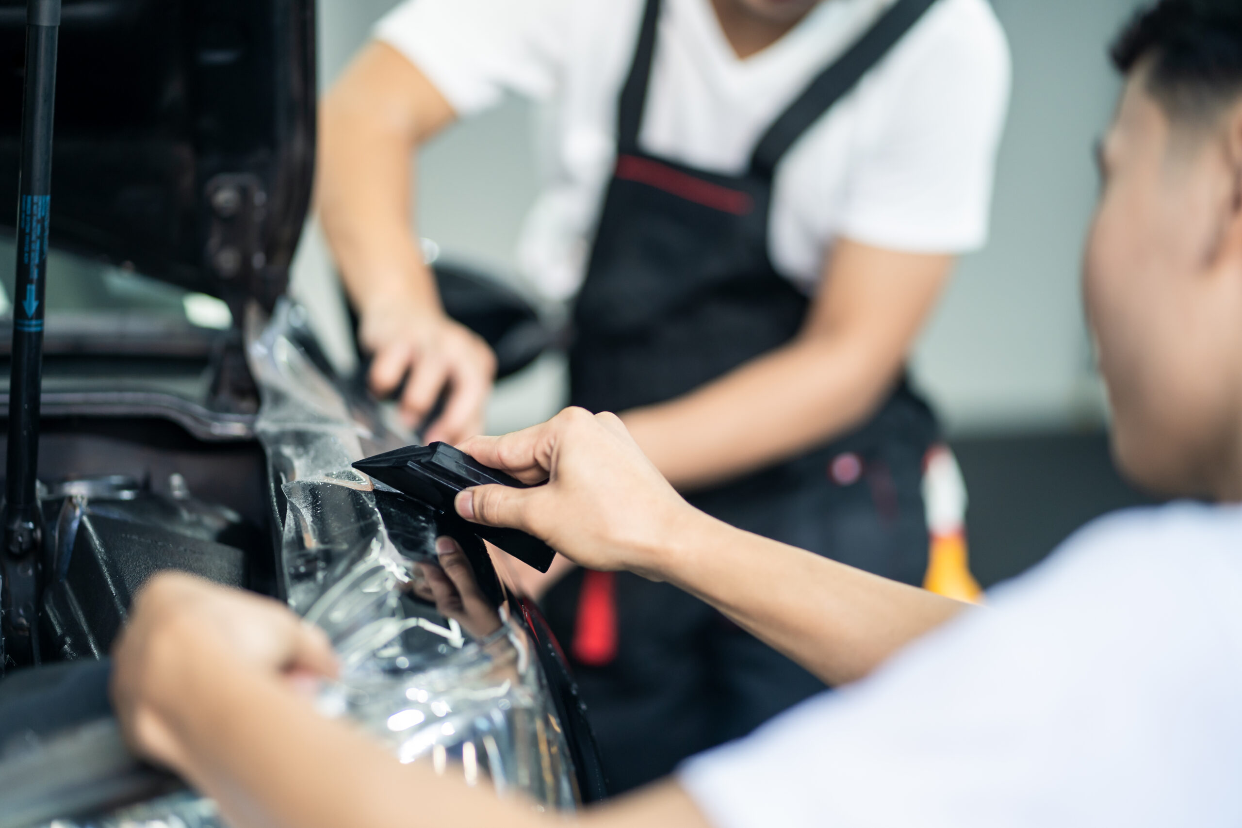 Focus on hand of worker holding film. Detailing of two male worker installing film to black color car in garage. Coating and protective for vehicle business concept clear bra protection.